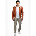 Man wearing a brown leather jacket with white shirt and beige pants on a white background