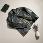 Black leather jacket with camouflage lining on a beige surface, next to a black notebook and a small vase with lavender.